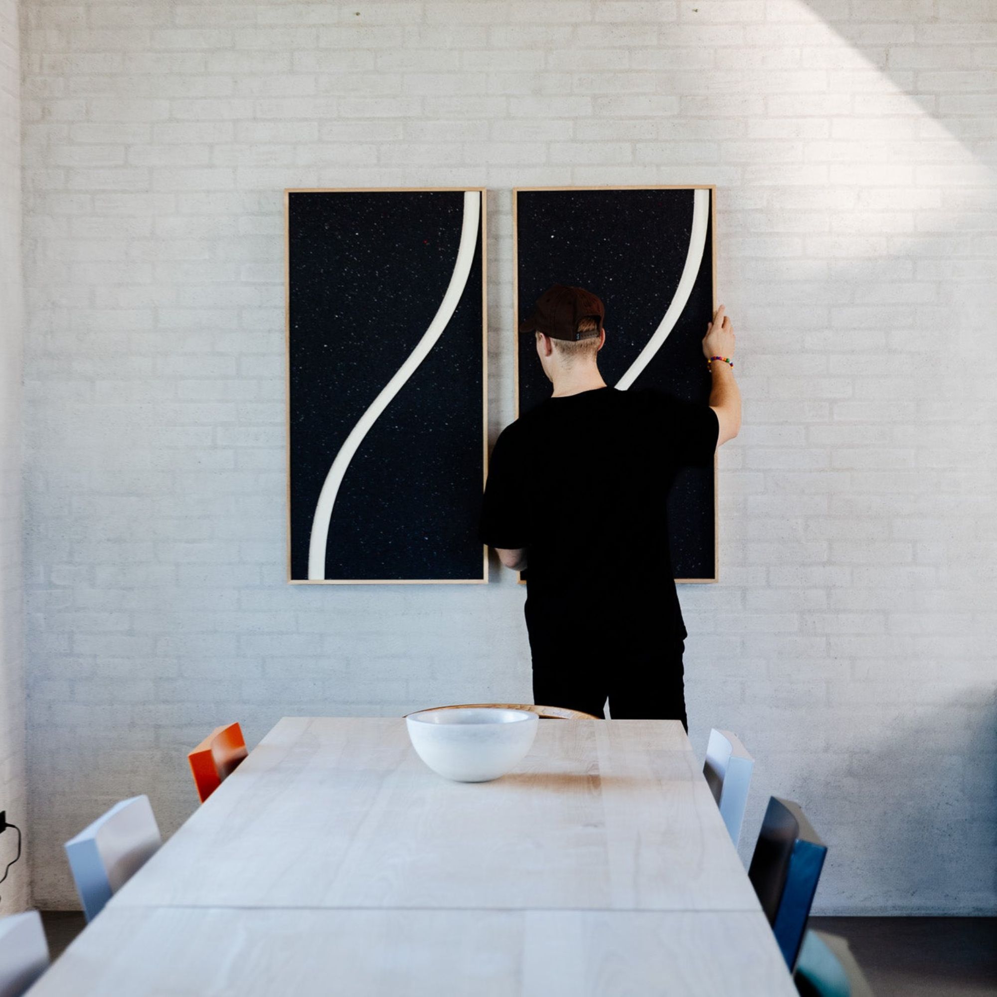 Man adjusting two decorative sound panels with curved lines above dining table in minimalist interior