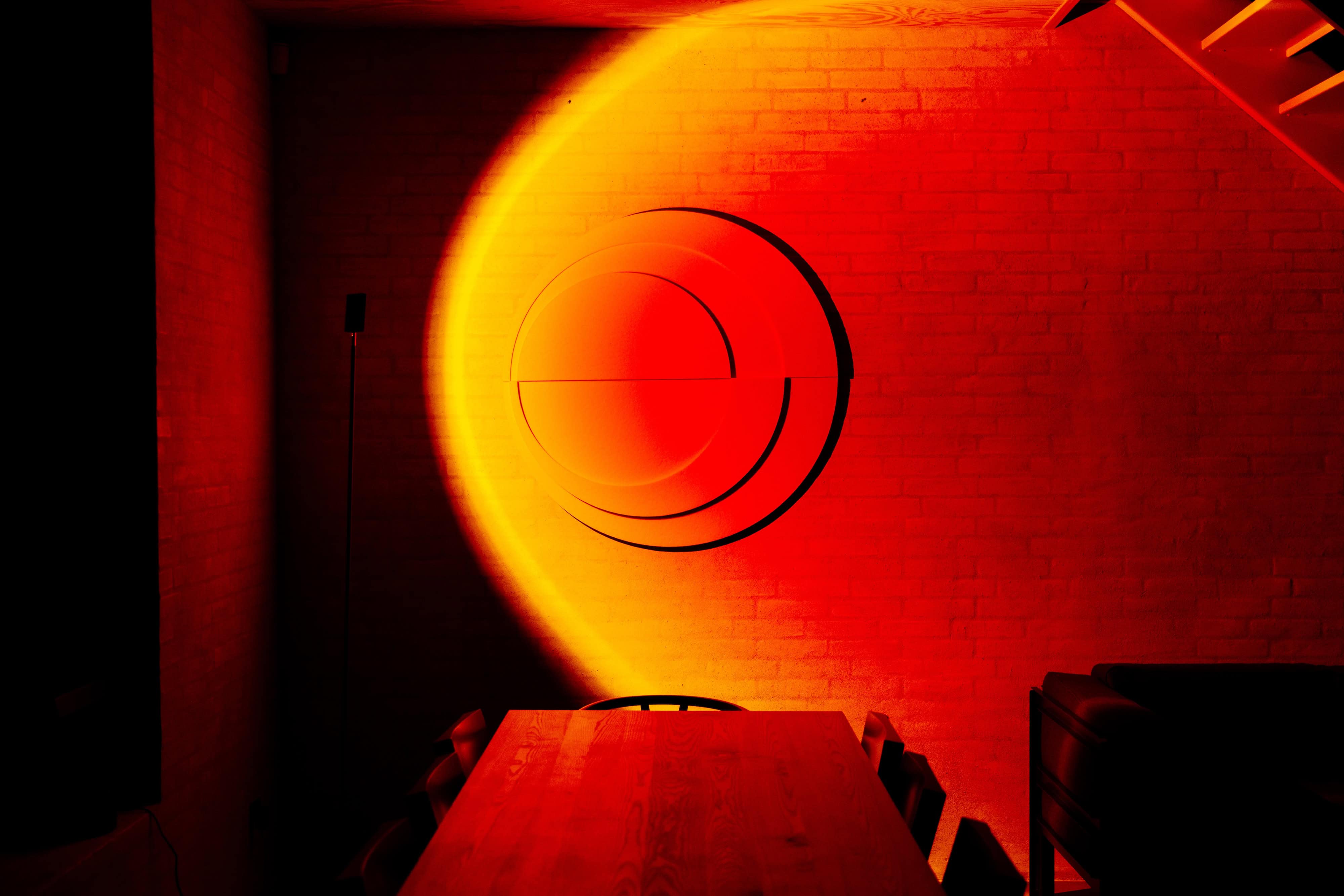 Decorative acoustic sound panel with circular design illuminated by warm orange lighting in modern dining room