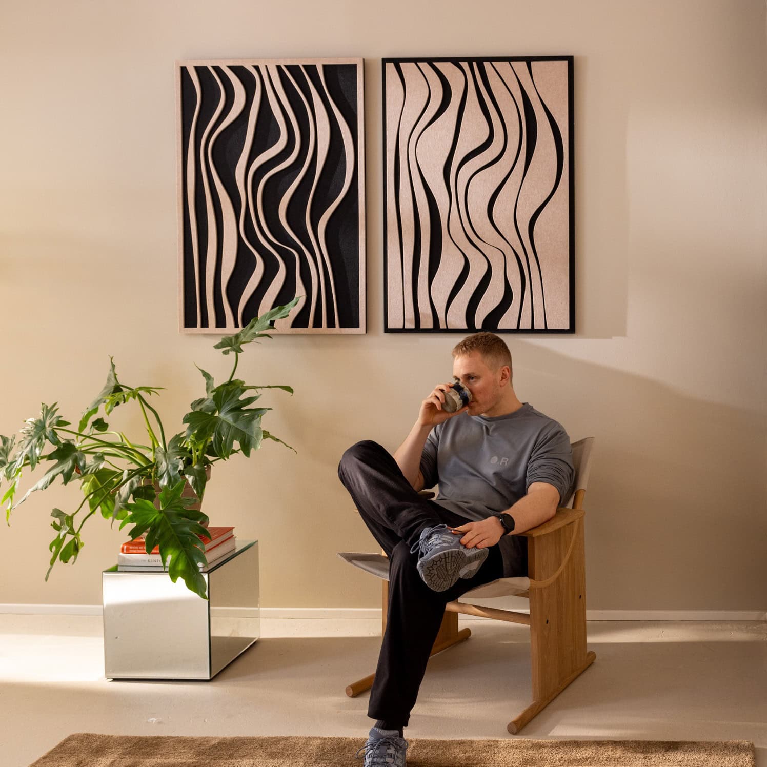 Man sitting with coffee beneath two decorative sound absorbing wall panels with organic wave pattern in living room